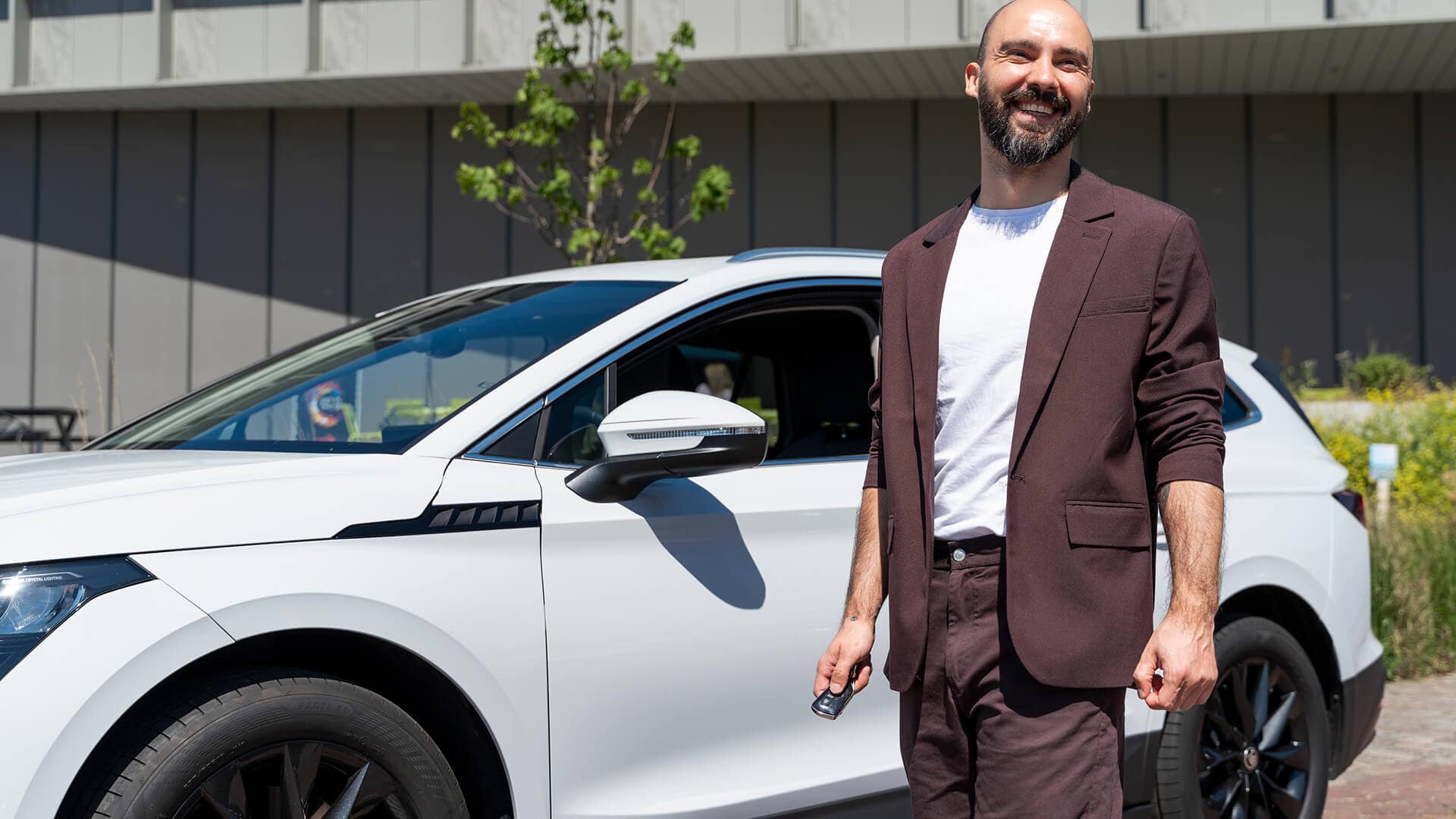 Man in pak bij witte auto lachend capaciteit private lease berekenen