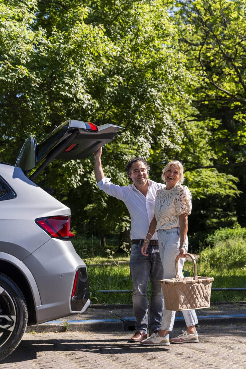 Stel berekent private lease en laadt picknickmand in kofferbak van auto