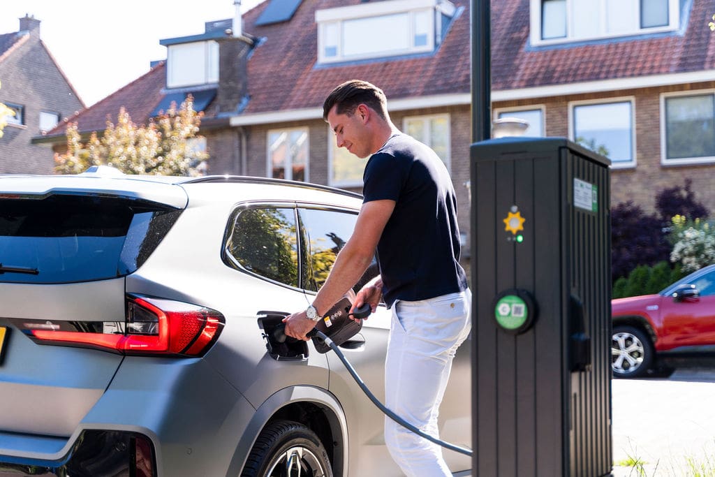 Man steekt stekker laadkabel in auto bij laadpaal